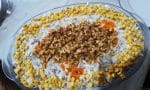 Renkli bir tabakta sunulan, erişte, yeşil mercimek, mısır ve kornişon turşu tanelerinin belirgin olduğu erişteli ve yeşil mercimekli yoğurtlu salata.