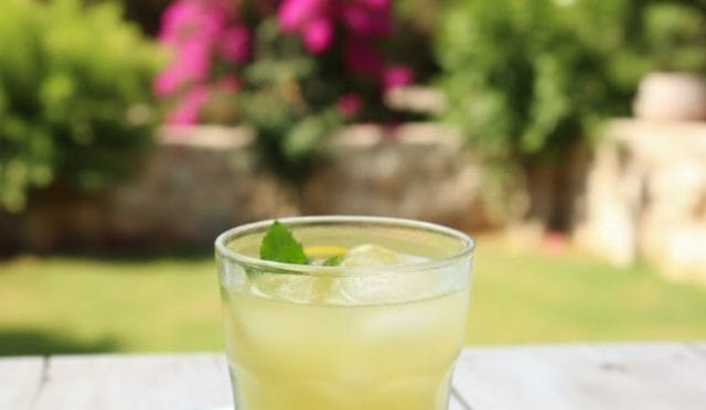 Taze nane ve fesleğen yapraklarıyla süslenmiş buzlu ev yapımı limonata bardağı.