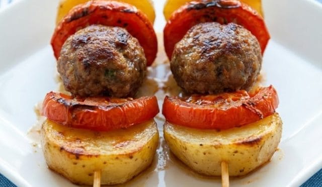Fırın tepsisine sıra sıra dizilmiş halka patates, domates, biber ve anne köftesi. Üzeri salça soslu fırında patatesli köfte yemeği pişmemiş hali/sunumu.