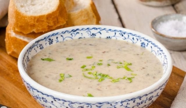 Lokanta usulü sütlü mantar çorbası tarifi sunumu. Mutfak masasında kaşık eşliğinde servis edilen, bol mantar taneli ve kremamsı dokulu çorba görseli.