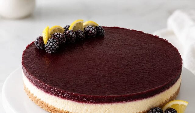 Dilimlenmiş, parlak çilek ve yaban mersini sosuyla kaplı, kremamsı dokulu, bisküvi tabanlı bir cheesecake.