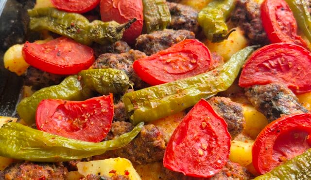 Fırında pişen köfteler ve patates dilimleri, yanında domates ve biberlerle servis edilmiş bir tepsi yemeği