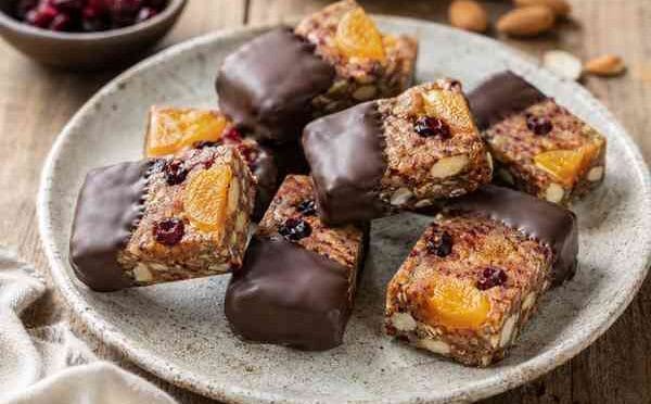 Dilimlenmiş, üzerinde kuru kayısı ve cranberry bulunan, yarısı bitter çikolataya batırılmış ev yapımı granola barlar.