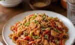 Taze sebzelerle zenginleştirilmiş, üzerinde taze soğan ve susam serpilmiş tavuklu noodle tabağı.