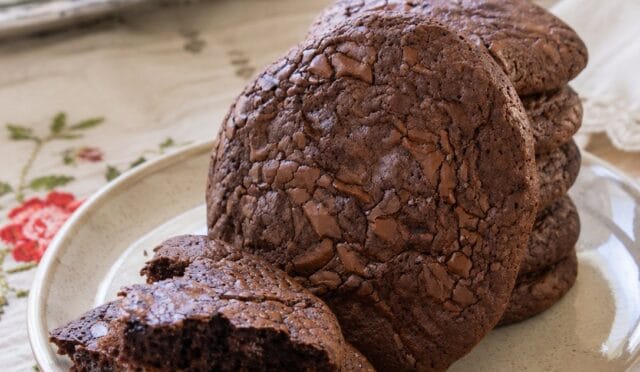 Fırın tepsisinde dizilmiş, üzeri çikolata parçalarıyla süslenmiş, hafif yayılmış yuvarlak çikolatalı brownie kurabiyeler.
