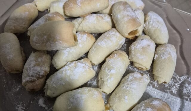 Üzeri pudra şekeri serpilmiş, elmalı ve tarçınlı rulo kurabiyeler yağlı kağıt serili tepside dizili.