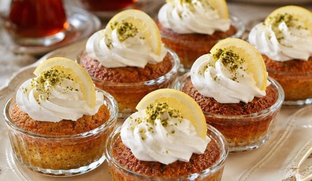 Muffin kalıplarında hazırlanmış, üzeri krem şanti ve Antep fıstığı ile süslenmiş, porsiyonluk limonlu ve mavi haşhaşlı revani dilimleri.