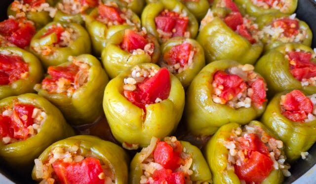 Tencerede pişmiş, üzeri domates dilimli, parlak ve lezzetli görünen kıymalı biber dolması